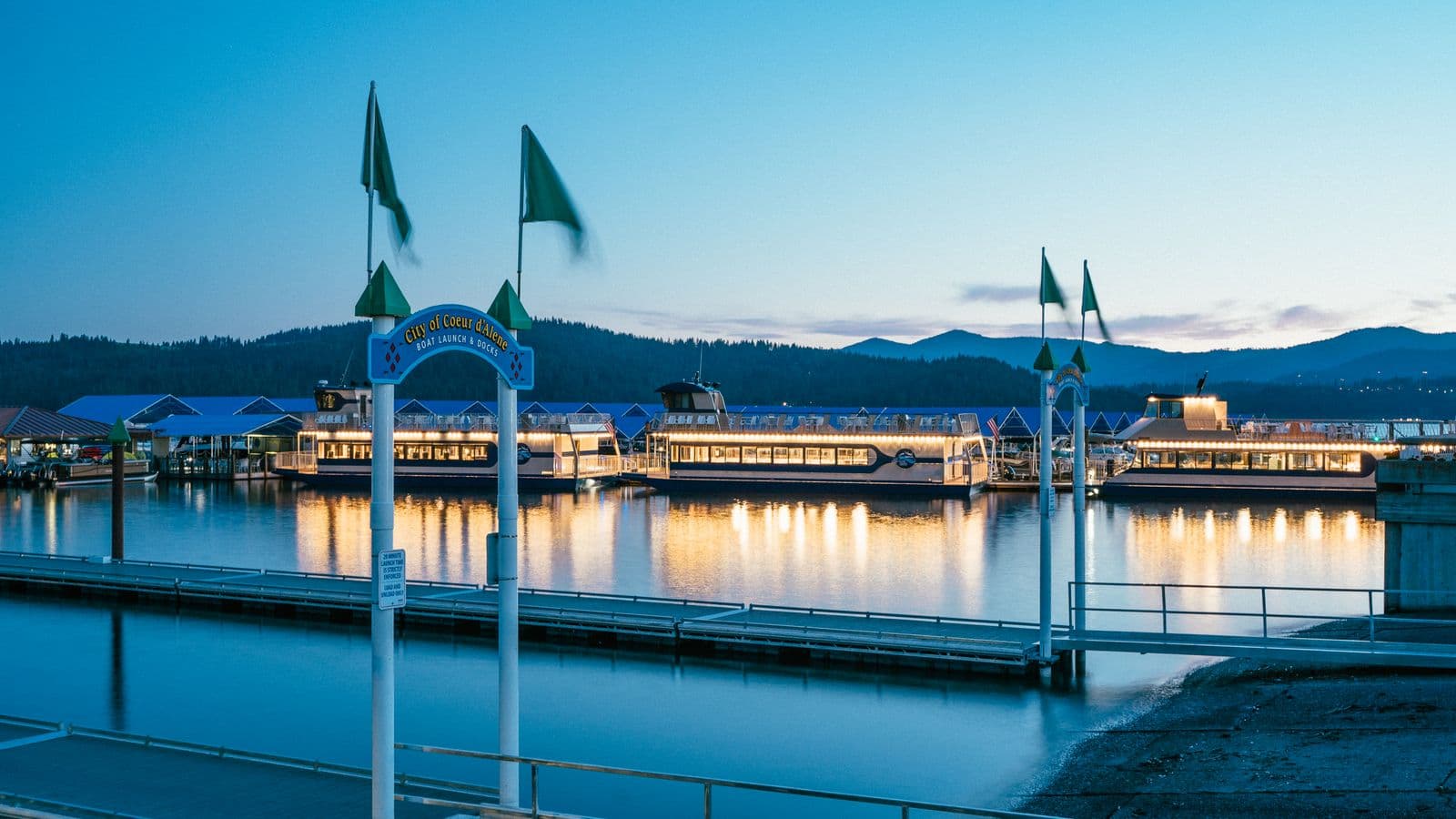 Coeur d'Alene city marina and boat docks lit at dusk with mountains behind the lake